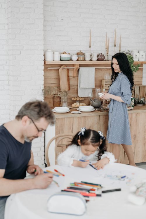 Free Father and daughter drawing while mother prepares food in a cozy kitchen. Stock Photo