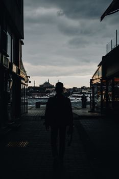 A striking silhouette of a man walking by the waterfront in Istanbul under moody skies.