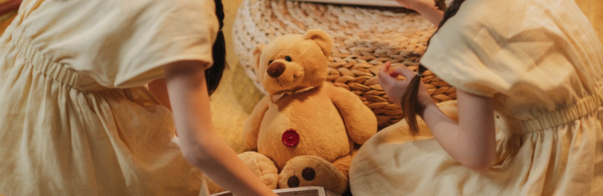 Two girls playing with toys on a woven carpet indoors, featuring a teddy bear and creative imaginati