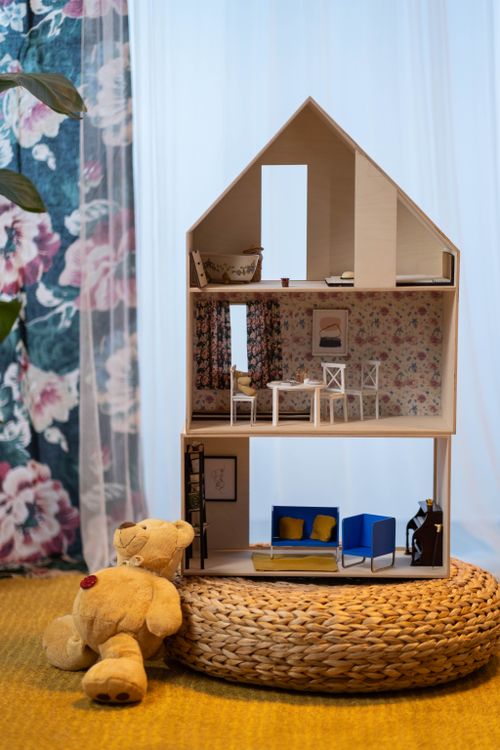 Tall miniature house with three furnished floors and a teddy bear sitting beside it for scale