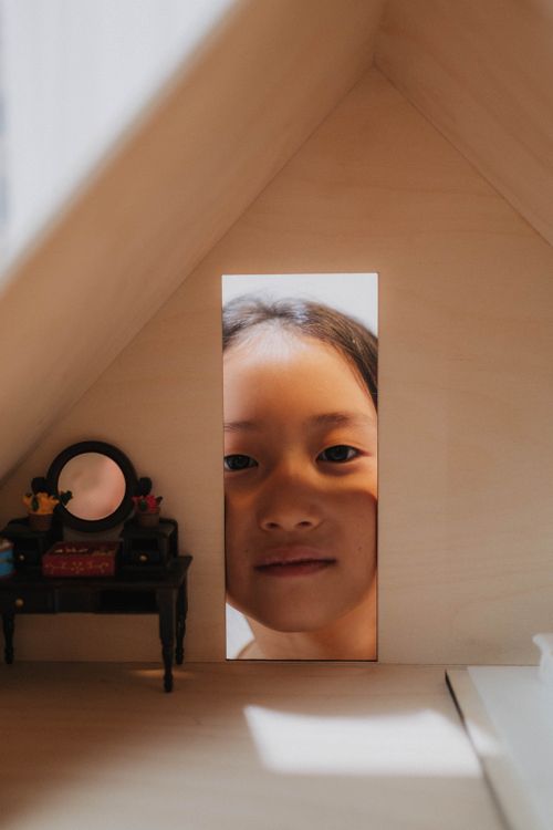 Free A child peeks through a dollhouse window, creating a playful and whimsical scene. Stock Photo