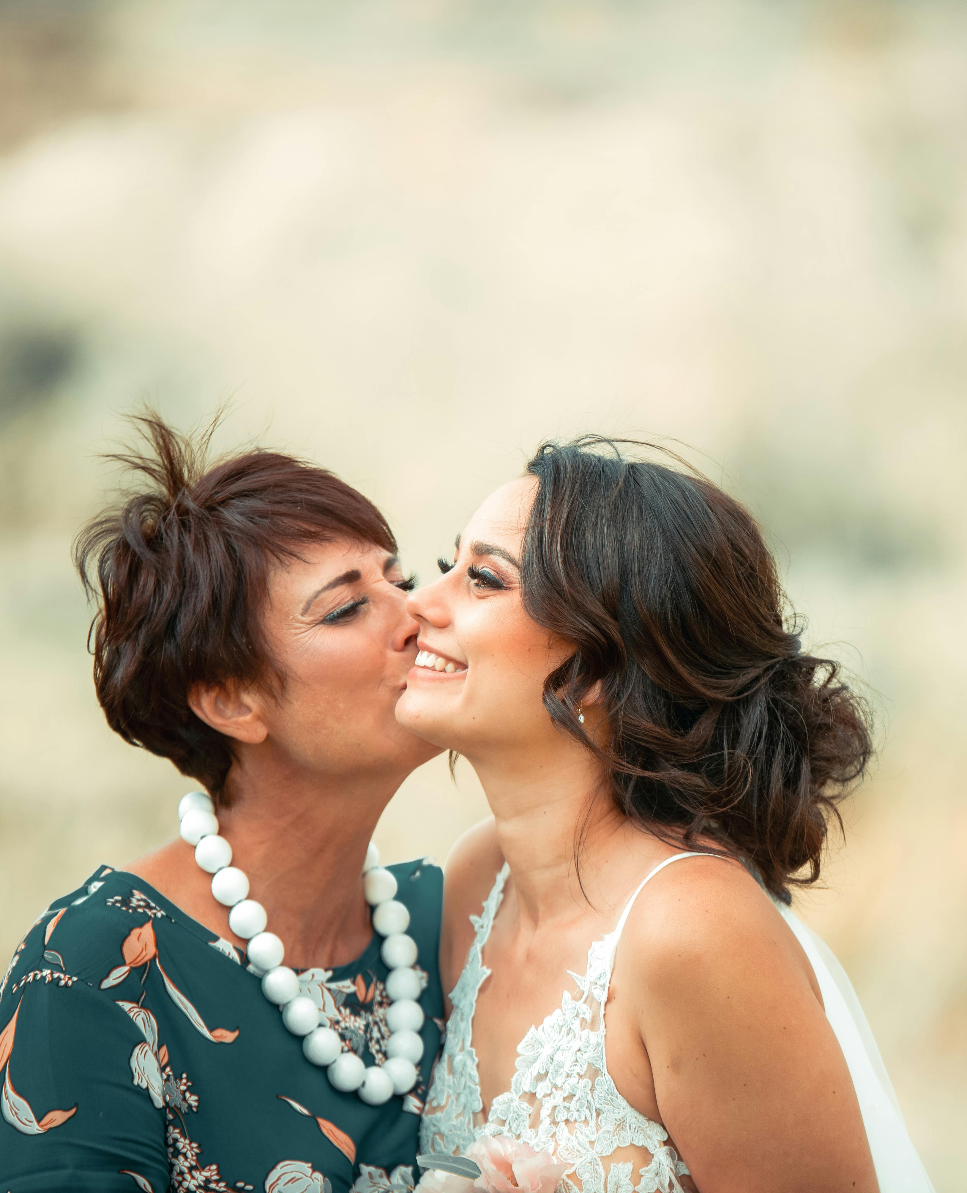 Candid moment of a mother kissing her daughter on her wedding day, showcasing love and joy.