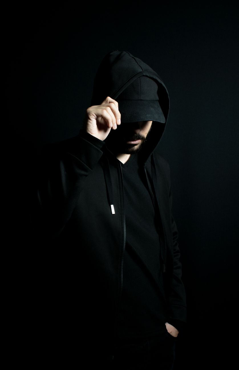 Stylish man in a black hoodie striking a mysterious pose in a studio setting.