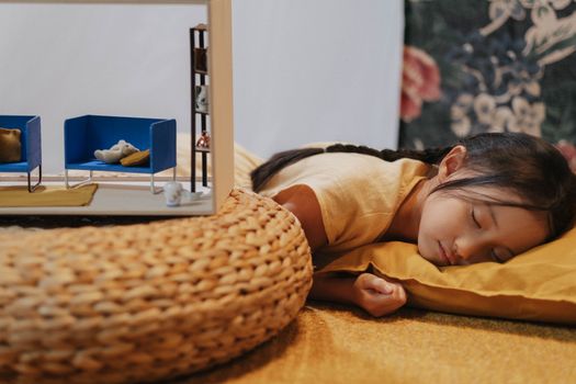 A young girl sleeps peacefully on a cushion indoors, showcasing a serene childhood moment.