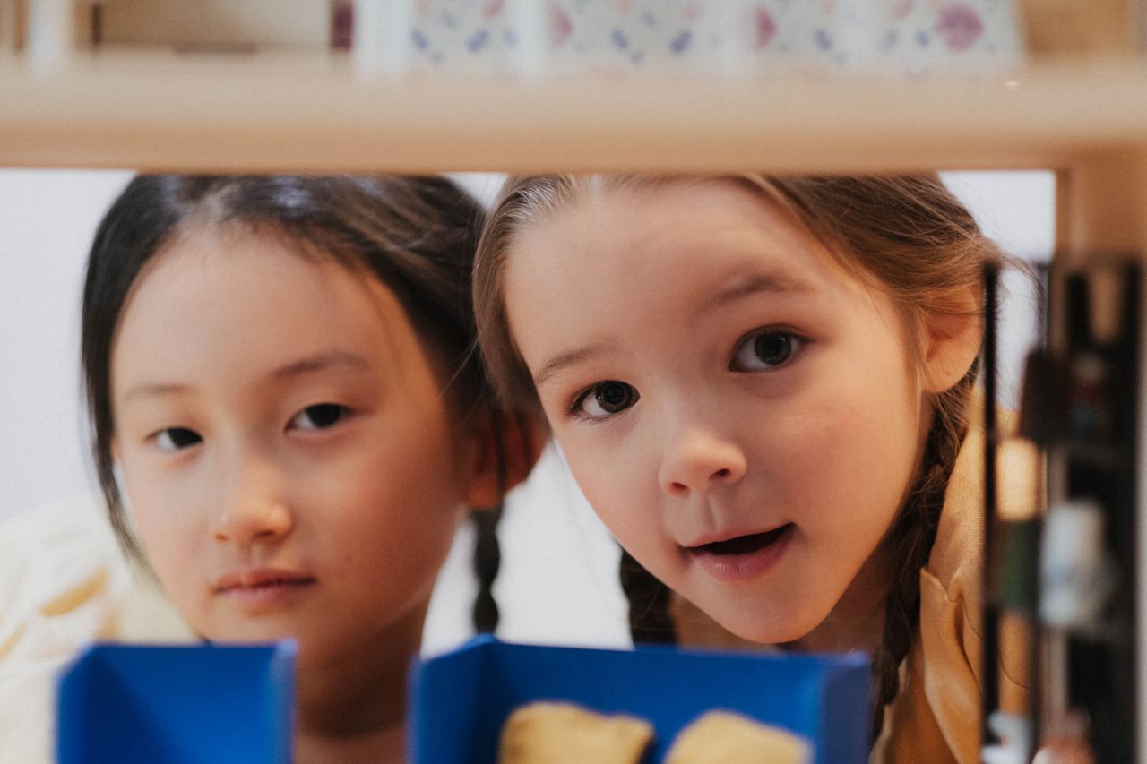 two girls exploring with curious expressions peering through shelves i