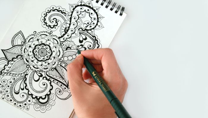 A hand drawing an intricate mandala pattern into a sketchbook — photo by Alena Koval on Pexels