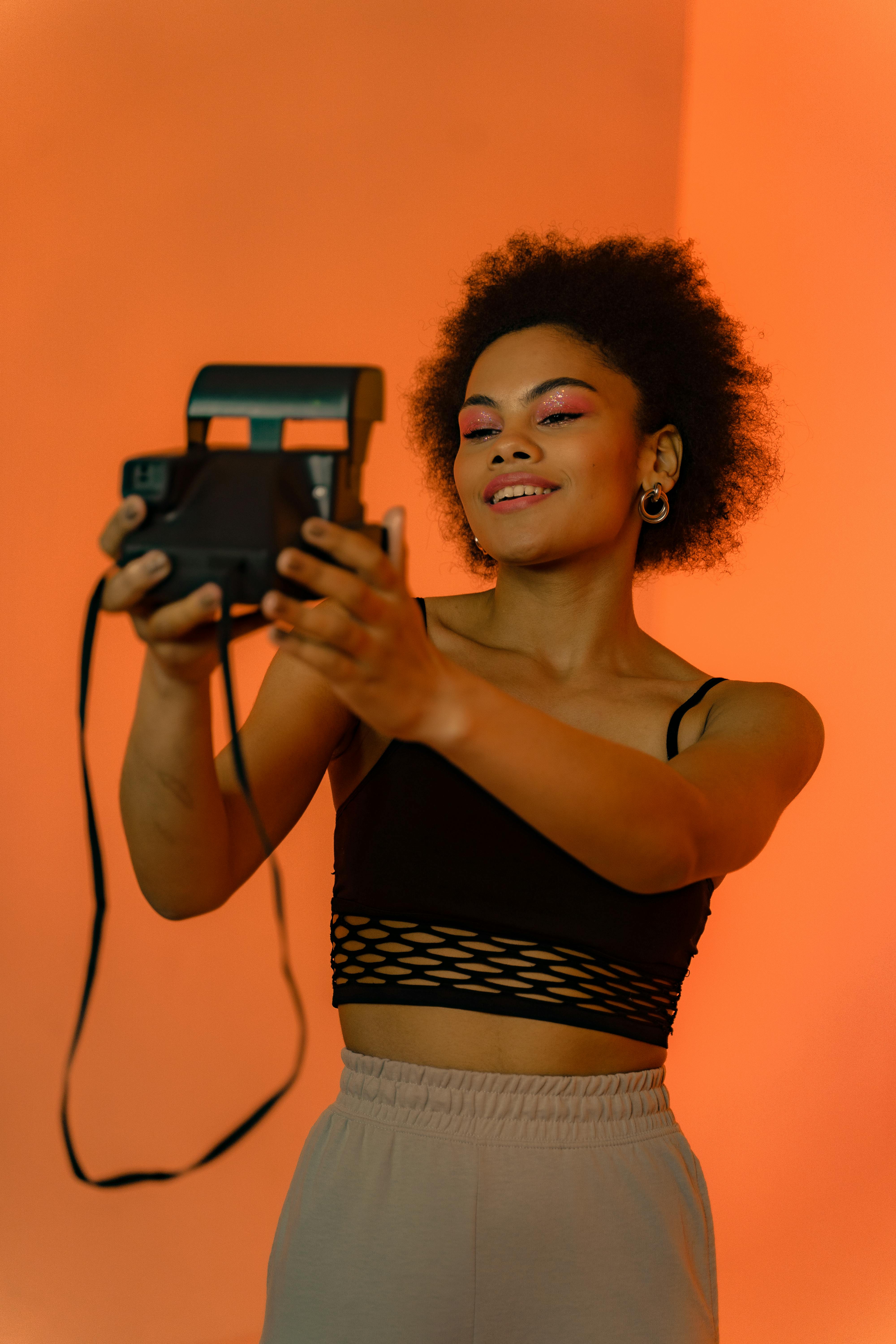 Stylish woman taking photos with a vintage camera against a vibrant background.