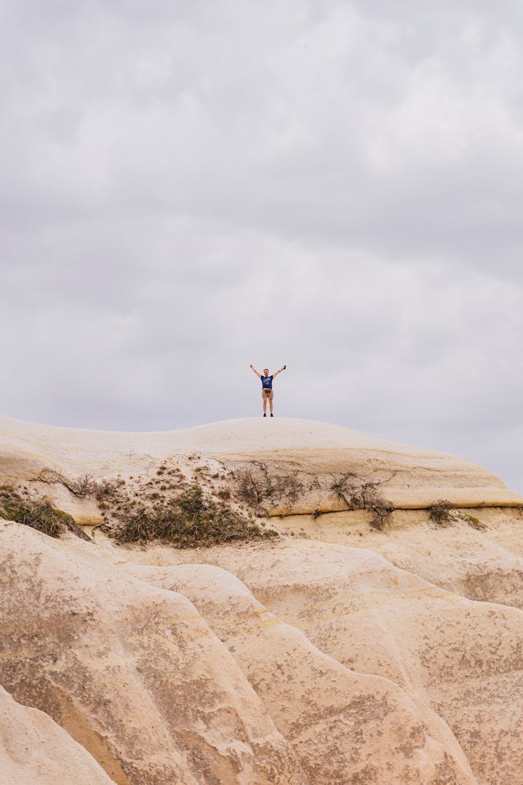 Man In Blue Shirt Standing On Brown Rock Formation Under White Clouds