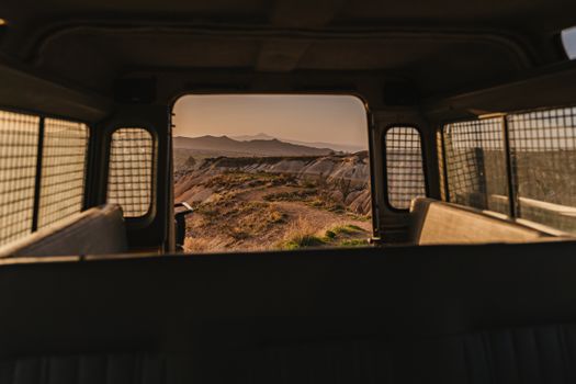 A dusty landscape viewed from inside a vehicle with mountains in the background at sunset.
