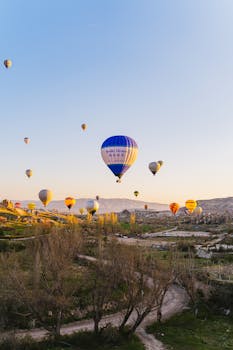 Colorful hot air balloons floating over stunning Cappadocia landscape at sunrise.