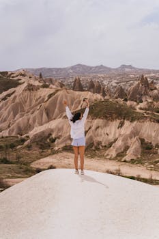 A woman raises her arms in triumph against the stunning rock formations of Cappadocia.