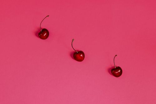 Free Minimalist food photo of three ripe cherries on a vibrant pink background, arranged in a flat lay style. Stock Photo