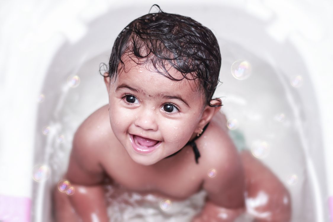 Free Picture of an Adorable baby enjoying a bath with bubbles, showcasing a joyful smile and playful expression. Stock Photo - Blog: Care of a baby (ears, hair, nails, and teeth)