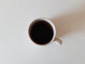 Simple ceramic mug filled with black coffee viewed from above on a white table.