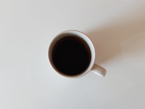 Simple ceramic mug filled with black coffee viewed from above on a white table.