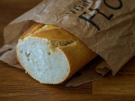 A freshly baked baguette partially wrapped in a paper bag on a wooden surface.