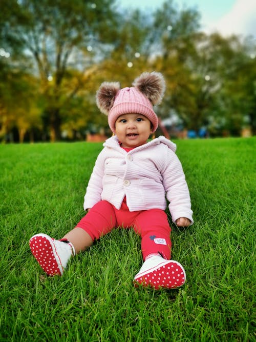 Child in Pink Jacket and Red Pants Sitting on Green Grass
