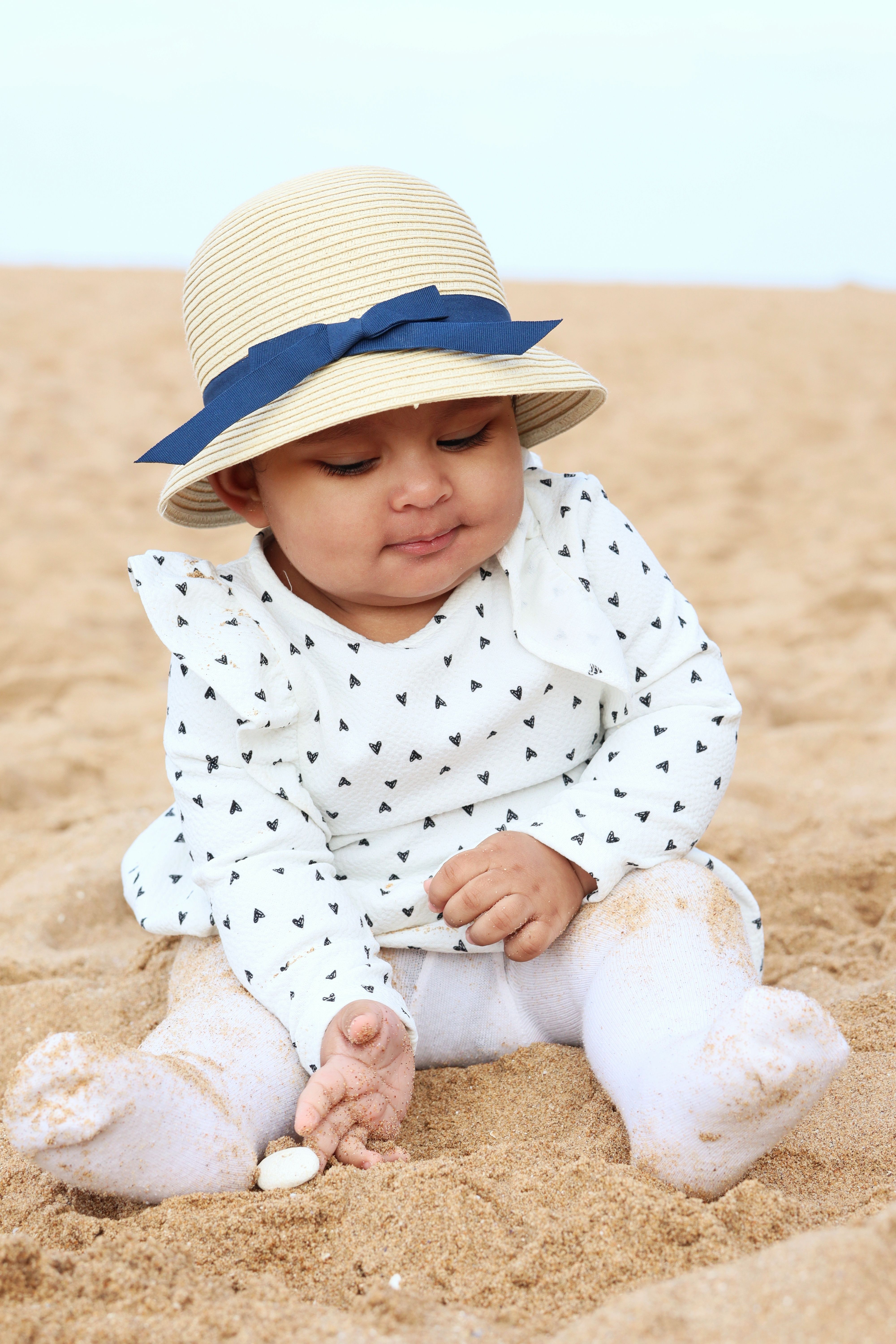 Bébé portant un chapeau assis sur le sable au bord de l’eau