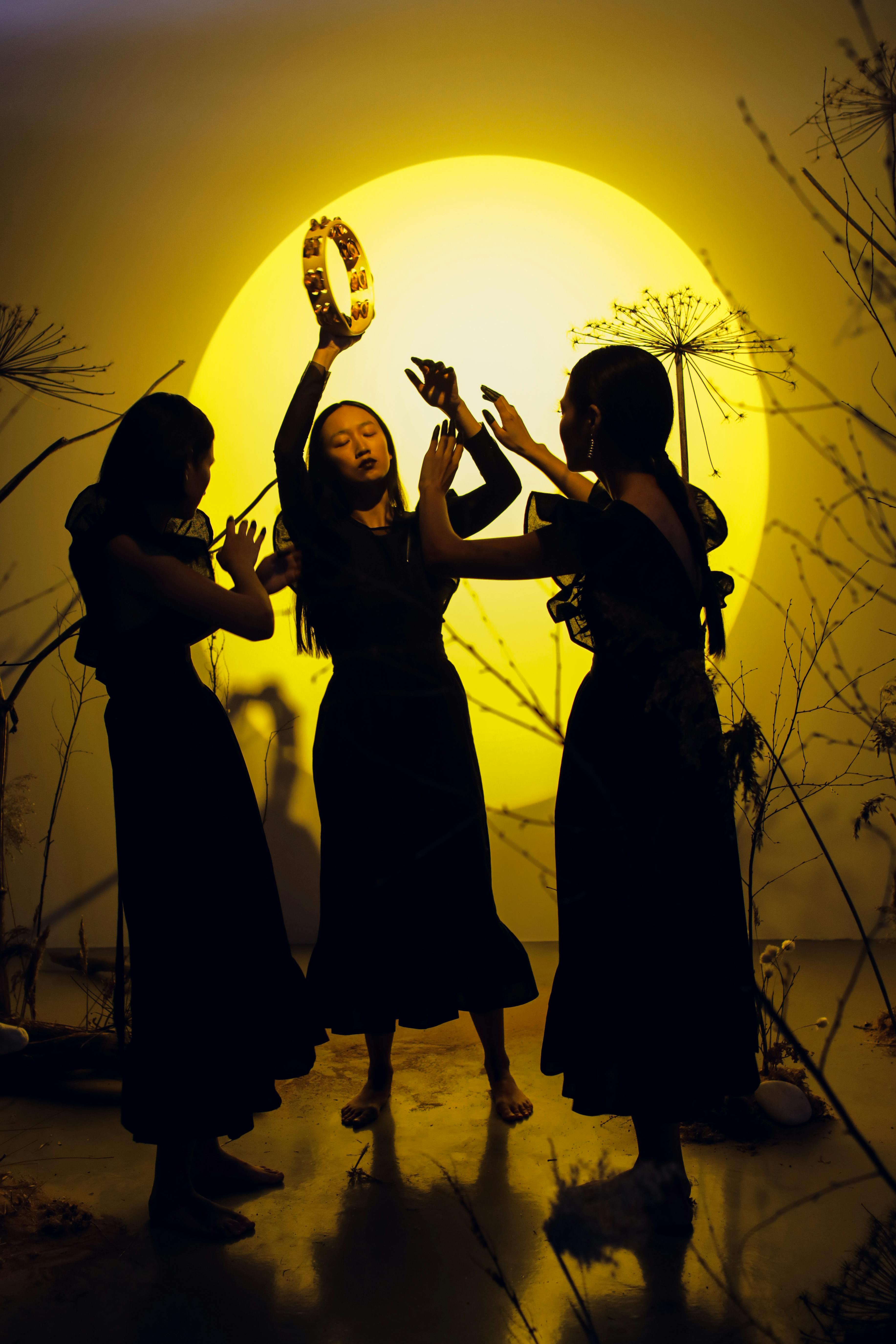 Free Three women dance with a tambourine under dramatic studio lighting, creating striking silhouettes. Stock Photo