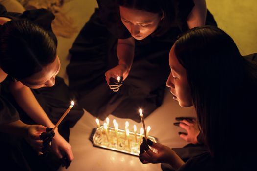 Top view of women holding candles in a dimly lit ritual setting, evoking spiritual themes.