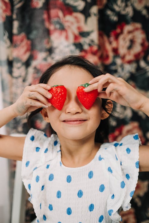 Girl in White and Blue Polka Dot Shirt Holding Red Strawberry