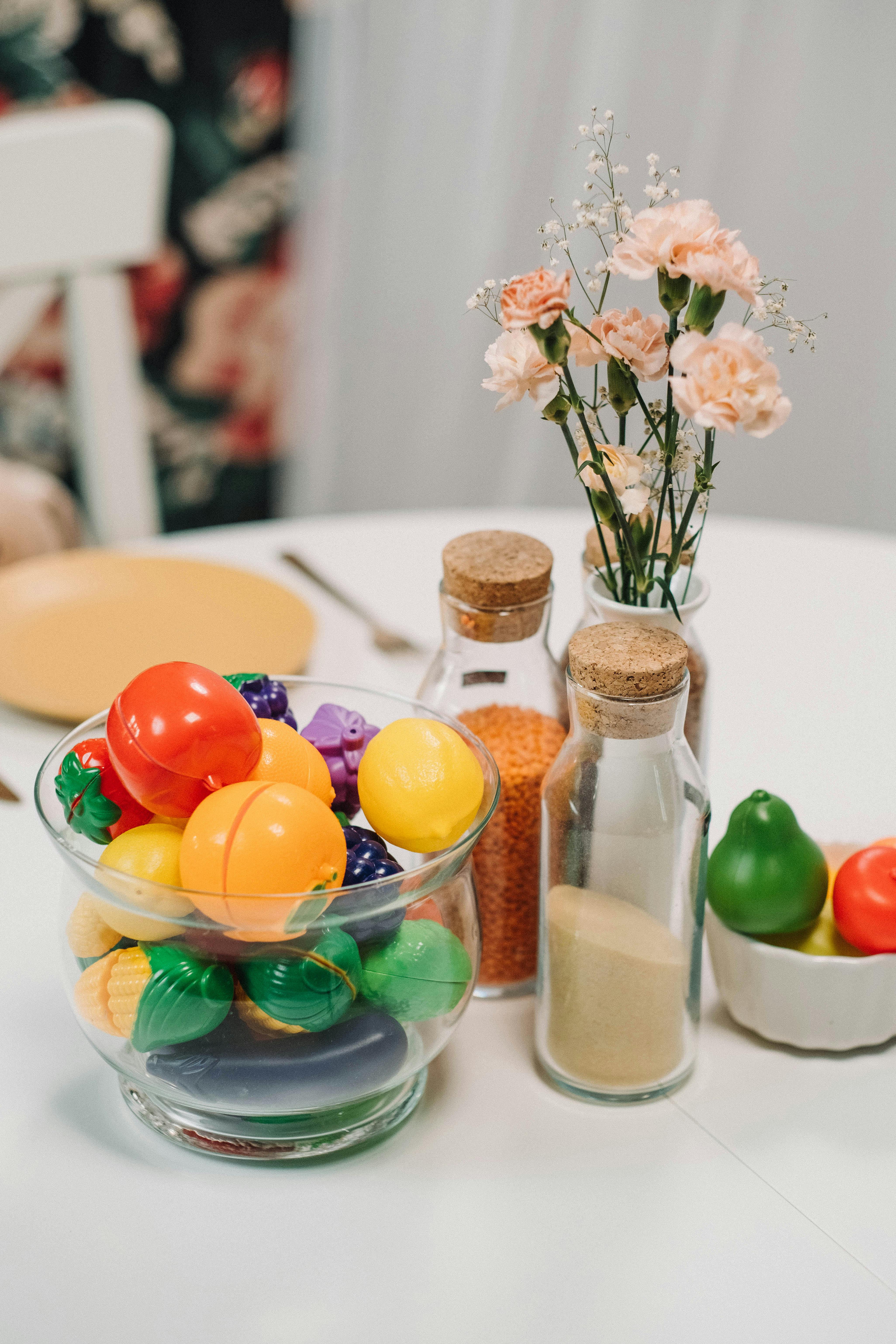 a glass bowl with plastic toys near the glass bottles and flower vase