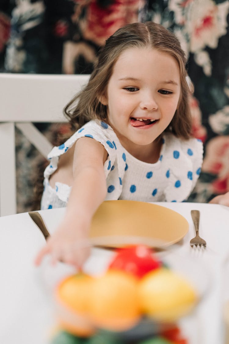 Girl In Polkadot Dress Sitting On Table With Plate