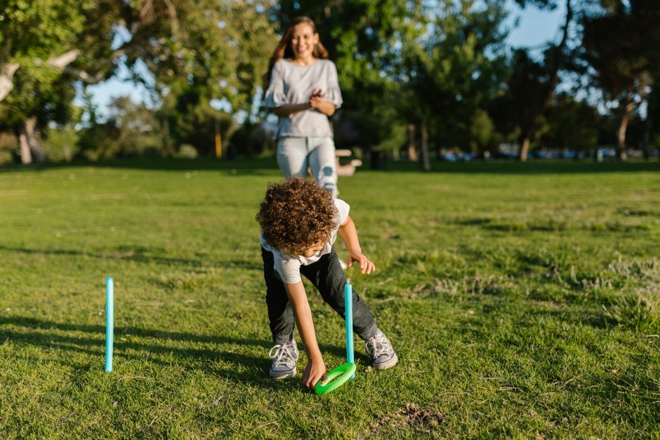 A mother and son enjoying a fun game of ring toss outdoors in a sunny park.
