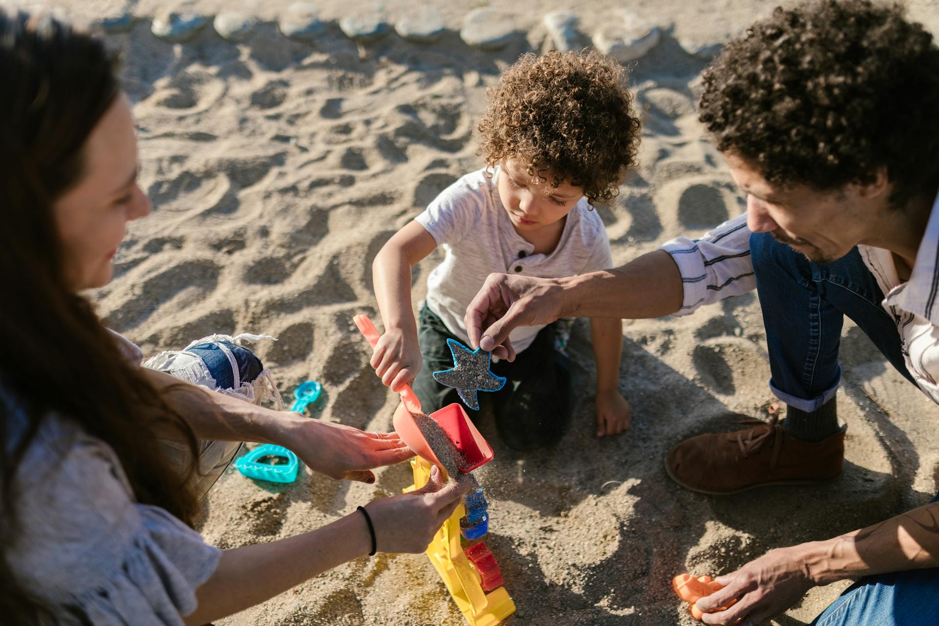 Parents and child playing with sand toys, enjoying quality time outdoors at the beach.