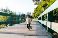Girl in White Shirt and Black Pants Running on Wooden Bridge