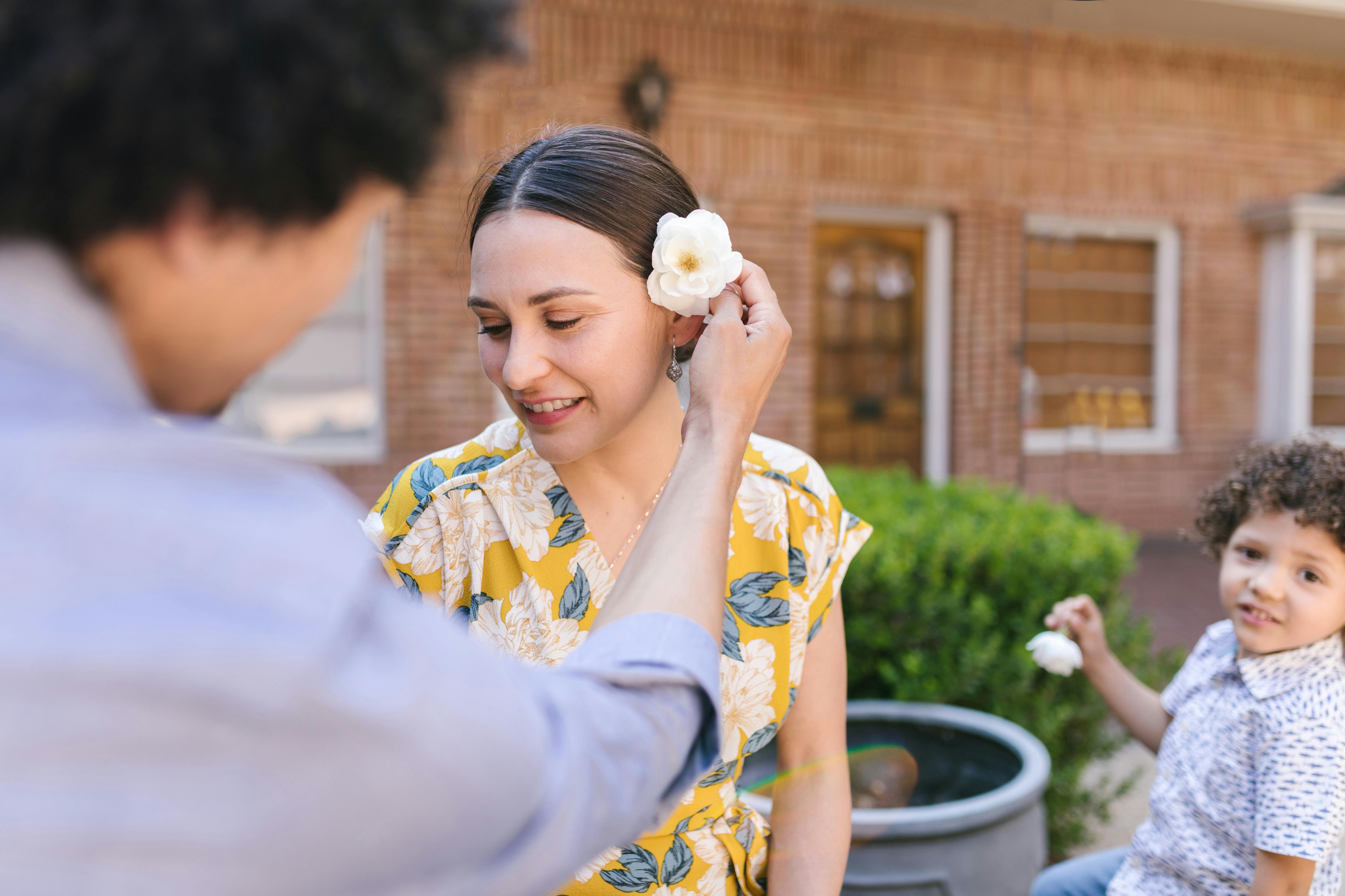 a person putting white flower on woman s ear
