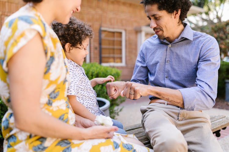 Family With A Little Son Sitting On A Bench Outside 