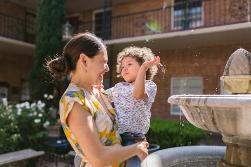 Free Son Splashing Water from the Fountain on His Mother  Stock Photo