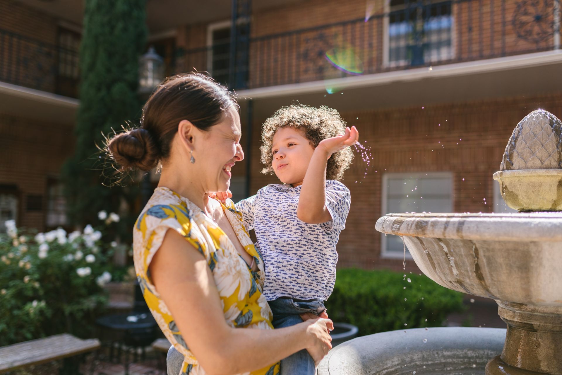 Mother and son share a happy moment by the fountain in a garden setting.