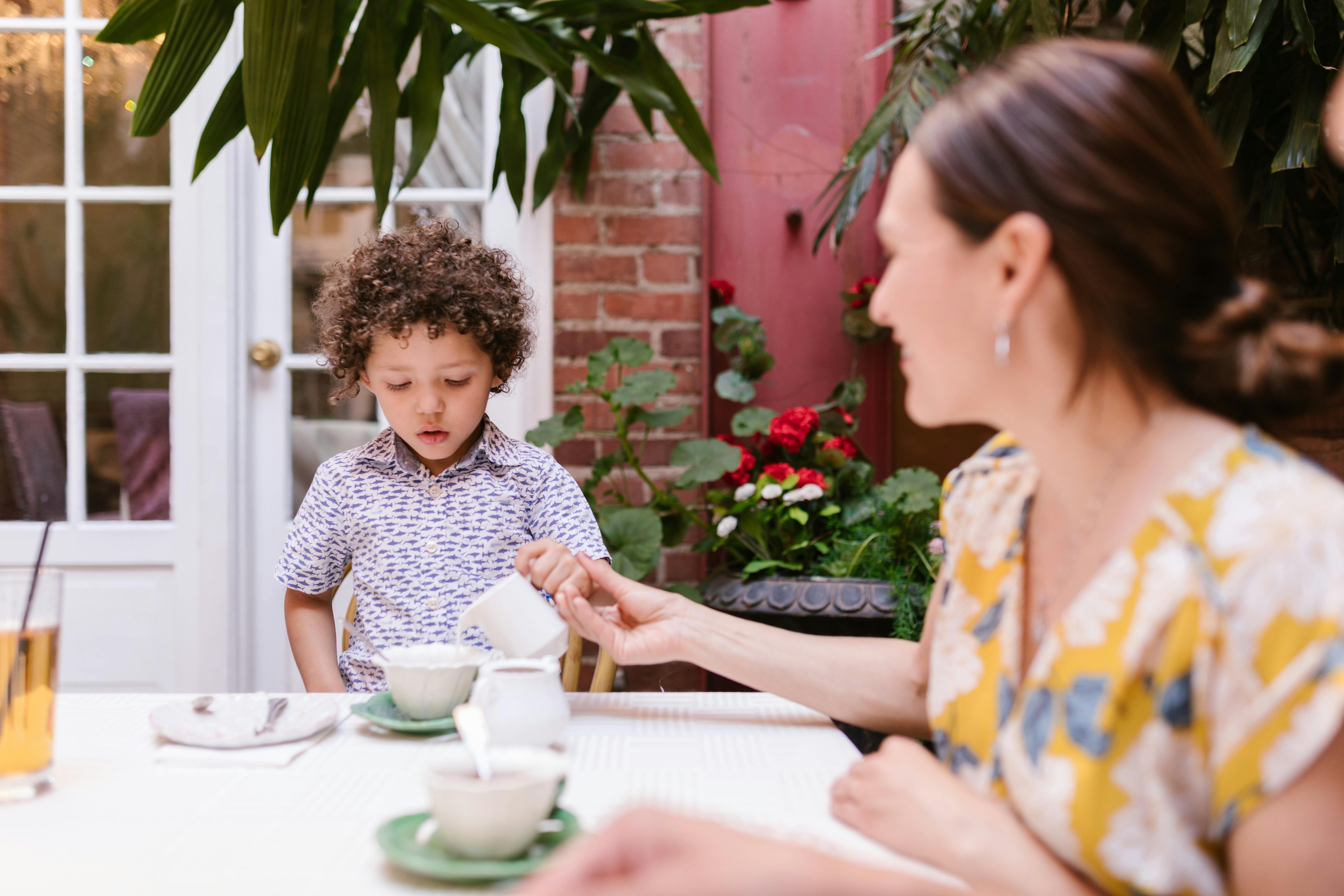 a mother in yellow blouse teaching her son how to pour drink on a cup