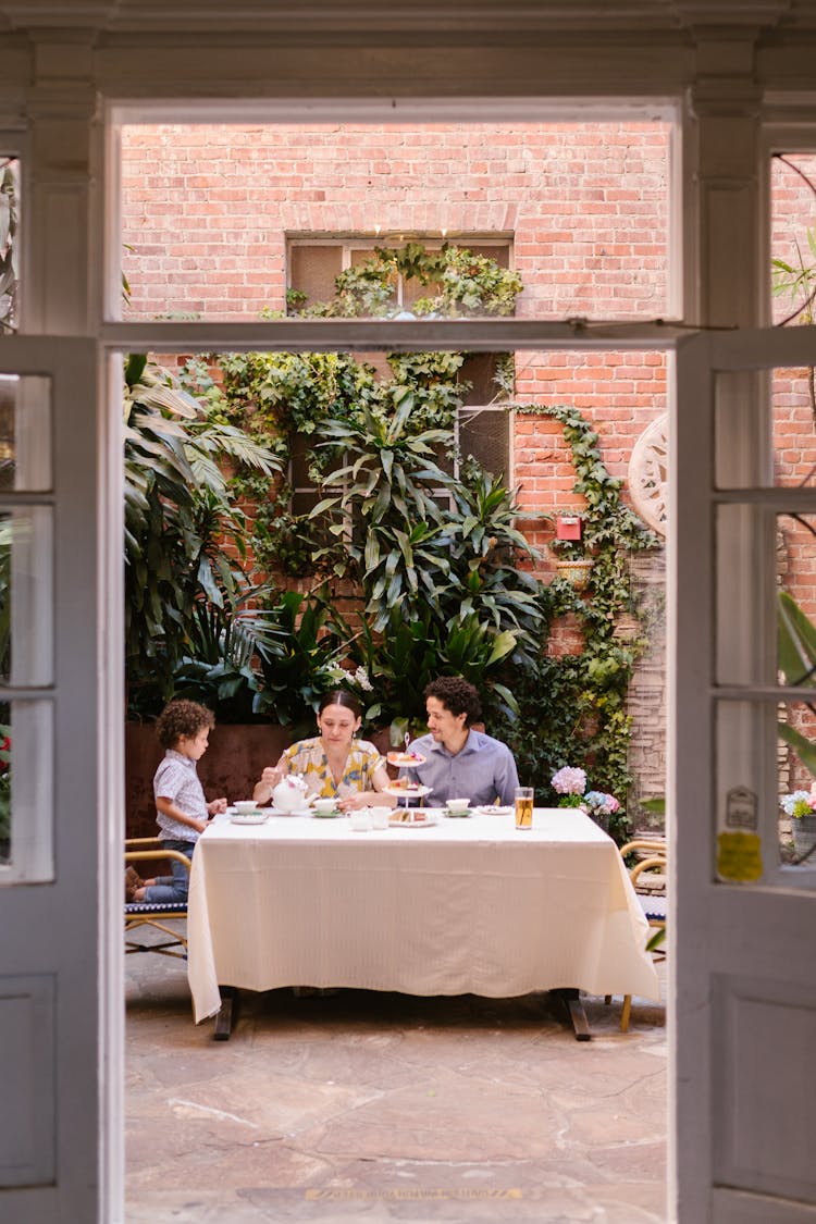 Family With A Little Son Sitting At The Table In A Restaurant Patio 