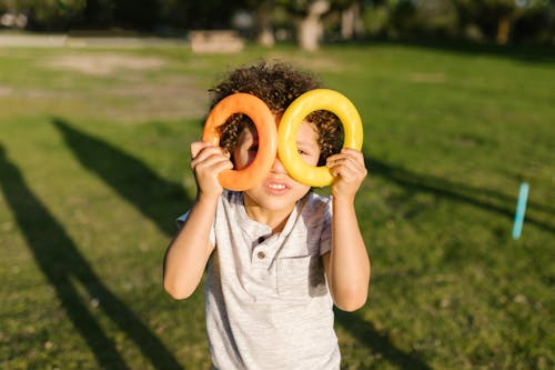 Young Boy in Gray Shirt Holding Round Plastic Toy Covering His Eyes