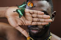 Artistic close-up of a man with butterflies on his hand and face, evoking natural beauty and elegance.