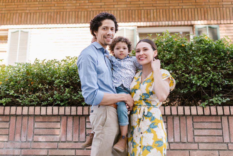 Familia sonriente de tres personas disfrutando de un día soleado al aire libre, capturando la felicidad y el calor.