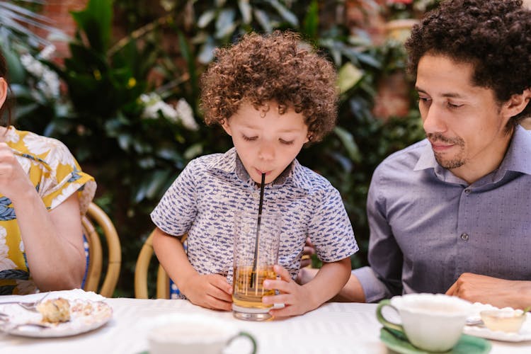 A Child Sitting Beside A Man At The Table Drinking A Beverage With A Straw