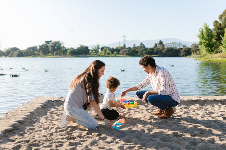 Family With A Little Son Playing In The Sand By The Water 