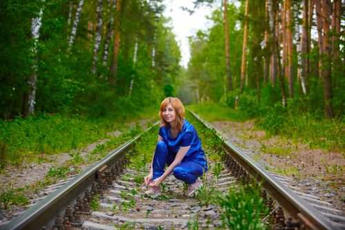 Free A woman squats on a forest railway track tying her shoelaces on a sunny day. Stock Photo