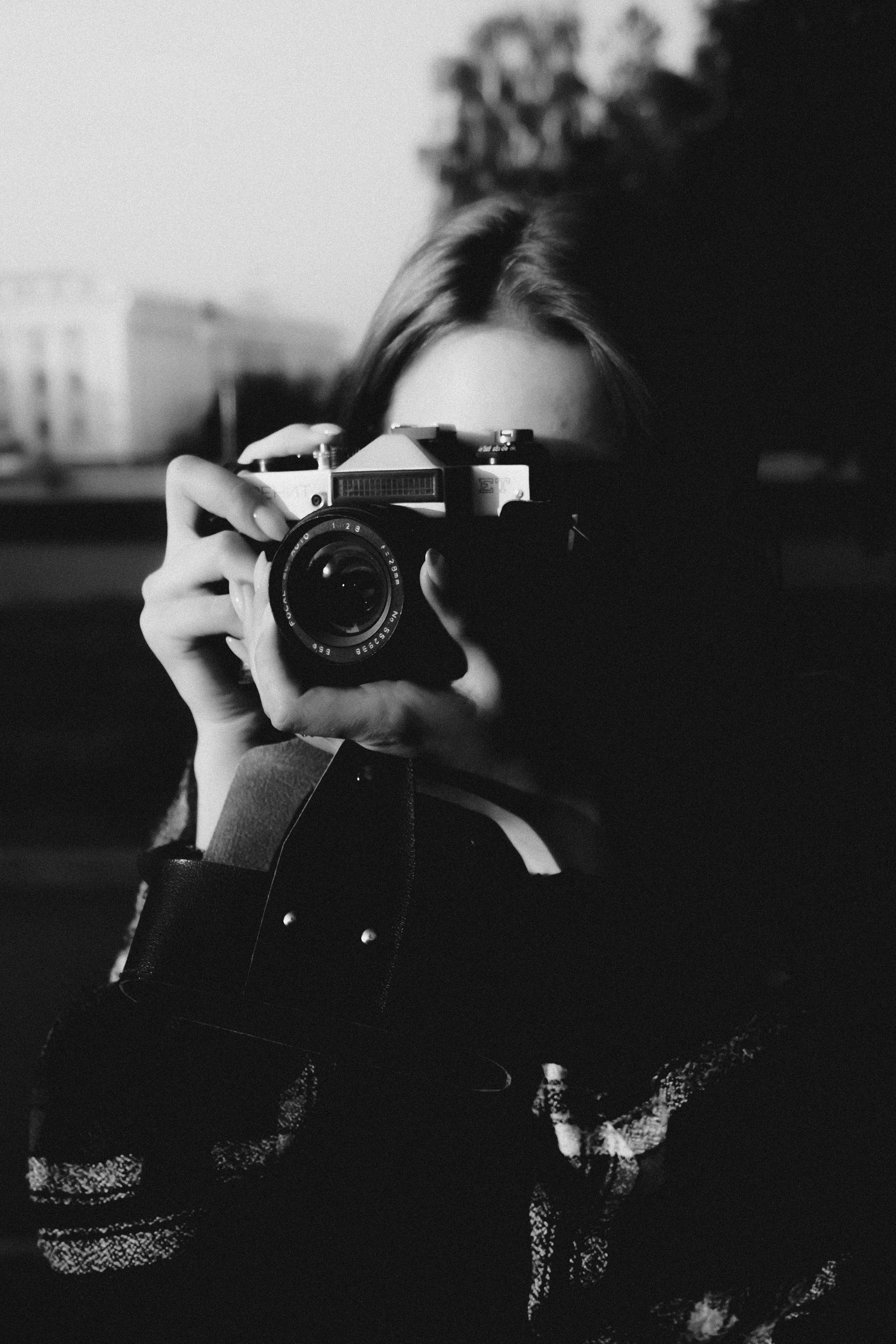 Black and white of unrecognizable female photographer taking photo on professional camera in city street