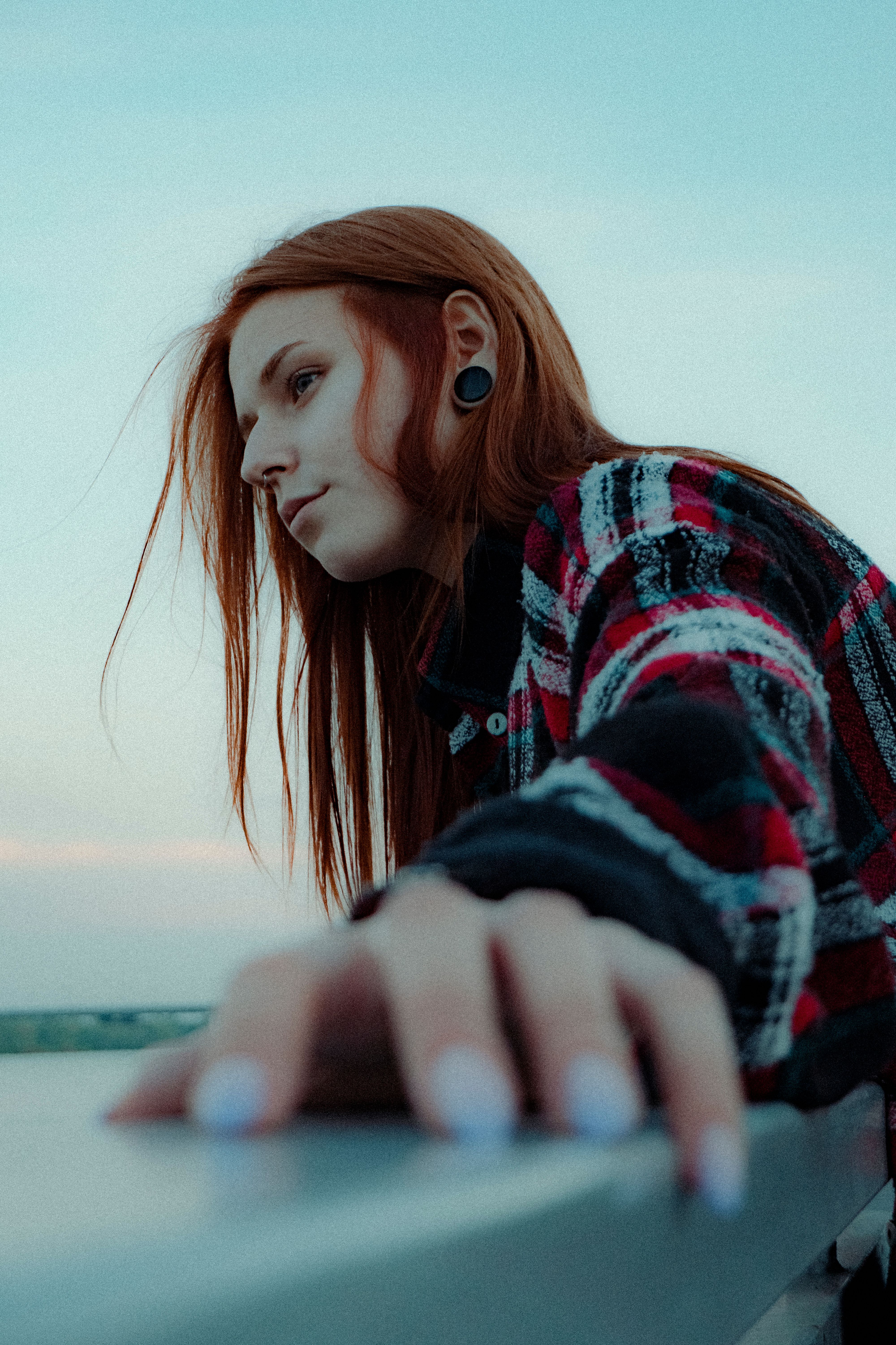 Caucasian woman with red hair in contemplation at dusk, wearing ear plugs.
