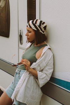 A stylish young woman leans against a camper wearing a striped bandana and casual outfit.