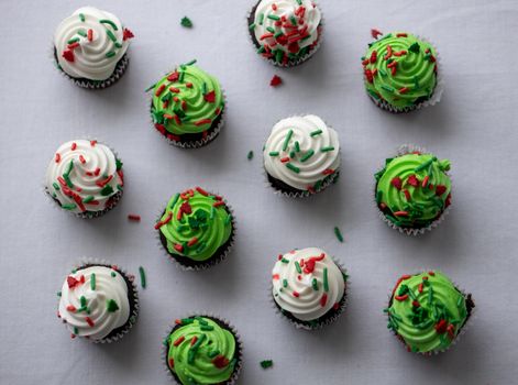 Top view of festive cupcakes with green and white frosting adorned with colorful sprinkles, perfect for holiday celebrations.