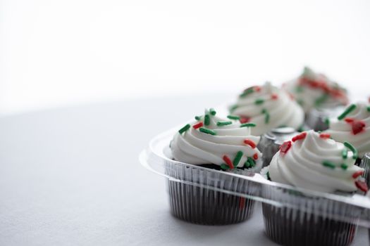 Close-up of cupcakes topped with white frosting and festive red and green sprinkles.