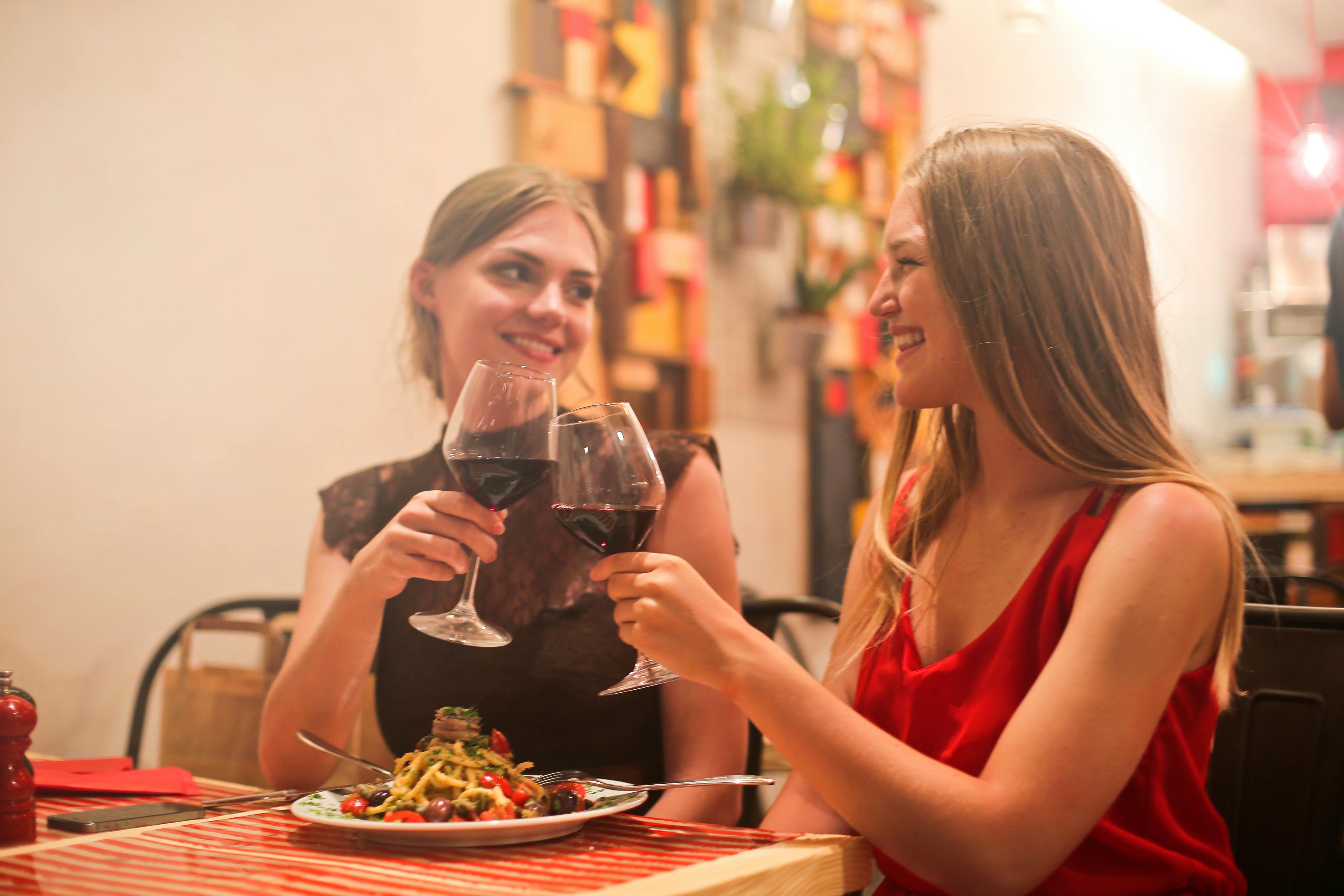 two women holding long stem wine glasses with red liquid