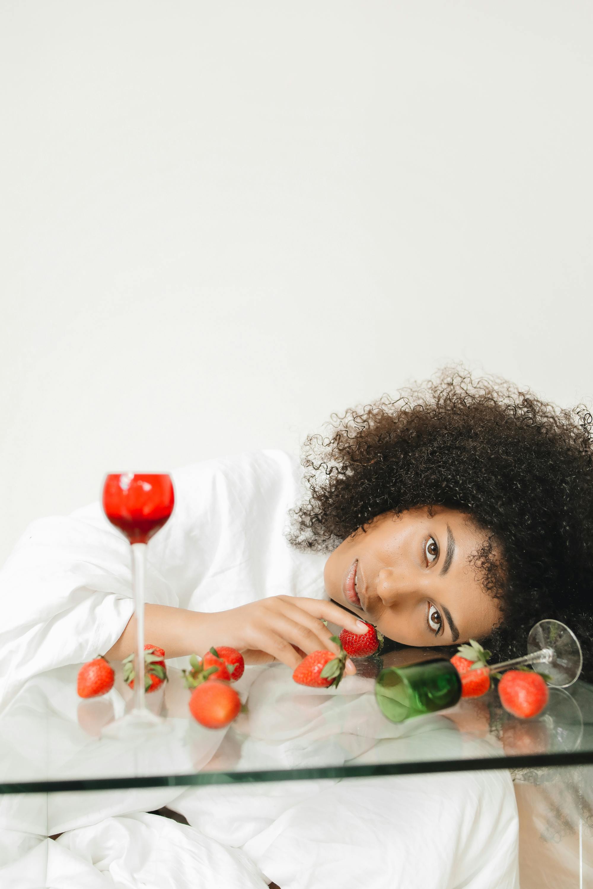 一位优雅的卷发女士在桌子上摆着草莓和玻璃器皿的姿势