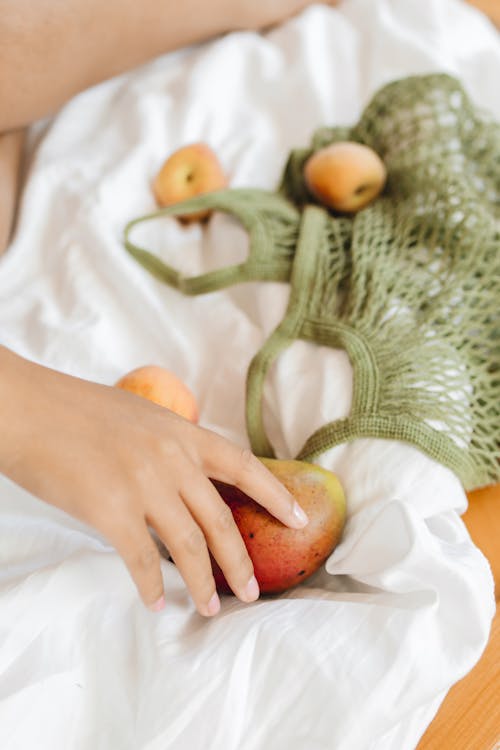 Person Holding a Fruit on White Textile